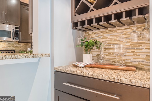 room details with light stone countertops, wet bar, stainless steel microwave, and decorative backsplash