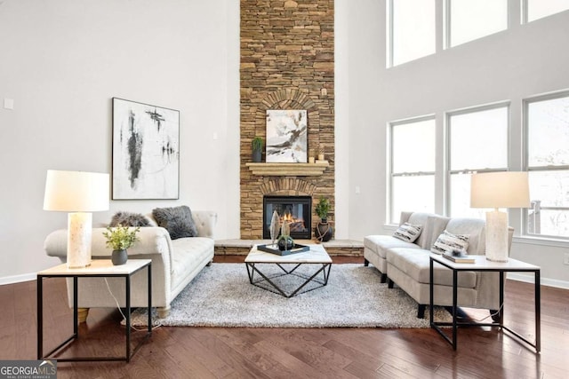 living room featuring a high ceiling, a stone fireplace, baseboards, and hardwood / wood-style flooring