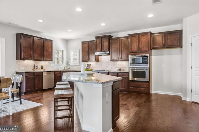 kitchen featuring under cabinet range hood, a kitchen island, appliances with stainless steel finishes, and dark wood-style flooring