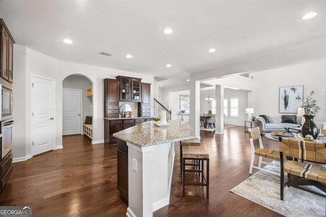 kitchen featuring light stone counters, dark wood-style floors, visible vents, glass insert cabinets, and dark brown cabinets