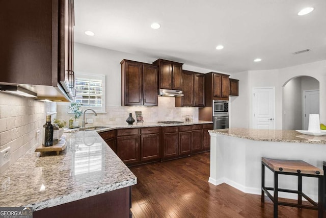 kitchen with dark wood-style floors, appliances with stainless steel finishes, a sink, and light stone counters