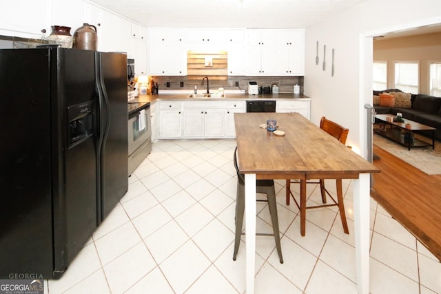 kitchen with light tile patterned floors, decorative backsplash, white cabinetry, a sink, and black appliances