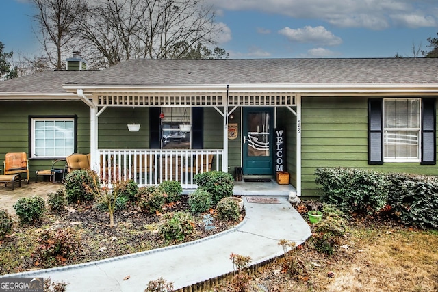 entrance to property with a porch, a chimney, and a shingled roof