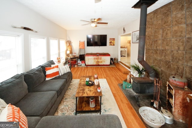 living area with a ceiling fan, wood finished floors, a wood stove, vaulted ceiling, and tile walls