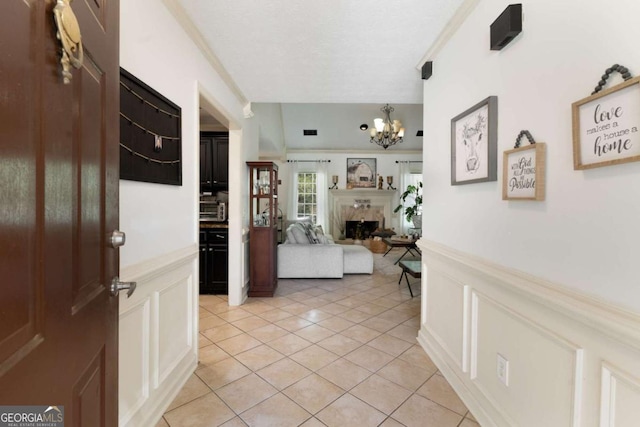 entryway featuring a wainscoted wall, a fireplace, a notable chandelier, light tile patterned floors, and a decorative wall