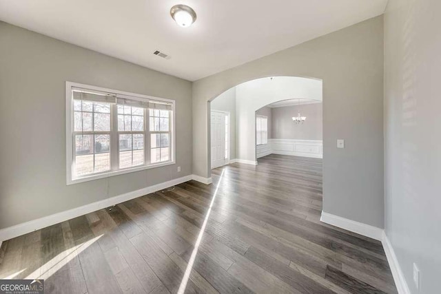 unfurnished room with a wealth of natural light, arched walkways, dark wood-style flooring, and baseboards