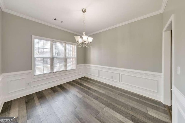 empty room with ornamental molding, a wainscoted wall, a notable chandelier, and dark wood finished floors