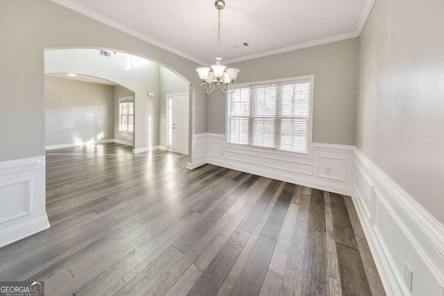 unfurnished dining area featuring arched walkways, ornamental molding, dark wood-style flooring, and a wealth of natural light