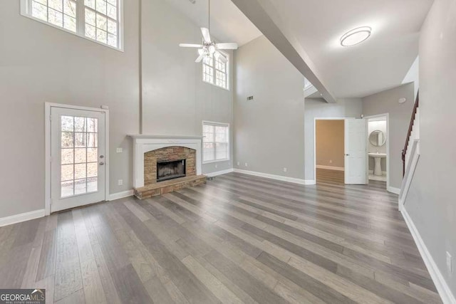 unfurnished living room featuring ceiling fan, a stone fireplace, wood finished floors, baseboards, and stairs