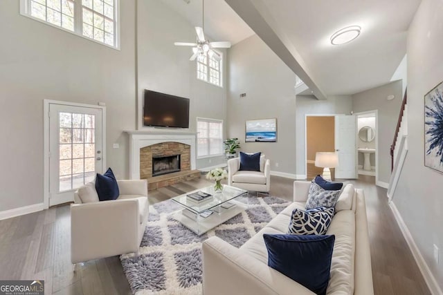 living area with a stone fireplace, wood finished floors, a towering ceiling, baseboards, and stairs