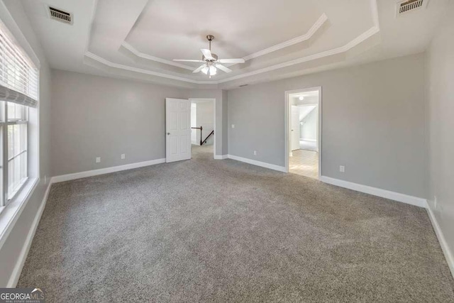 unfurnished bedroom with carpet floors, a tray ceiling, crown molding, visible vents, and baseboards