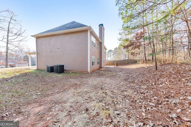 view of property exterior featuring central AC, fence, and a chimney