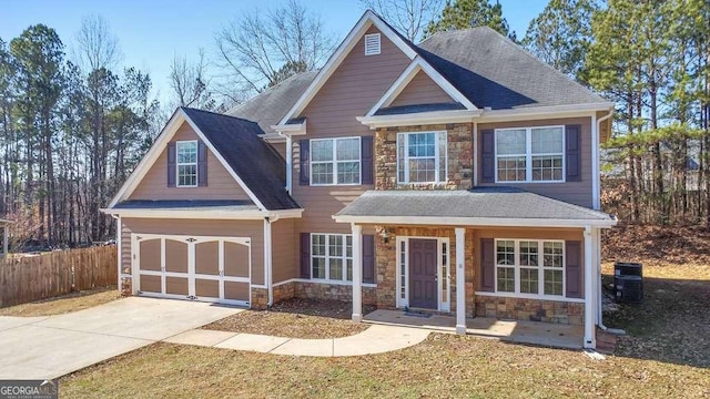 craftsman inspired home with a shingled roof, stone siding, fence, and driveway