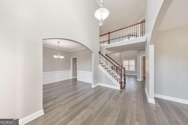 unfurnished living room with arched walkways, crown molding, a high ceiling, wood finished floors, and stairs