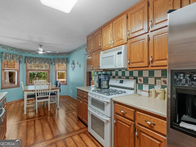 kitchen featuring brown cabinets, tasteful backsplash, light countertops, light wood-style floors, and white appliances