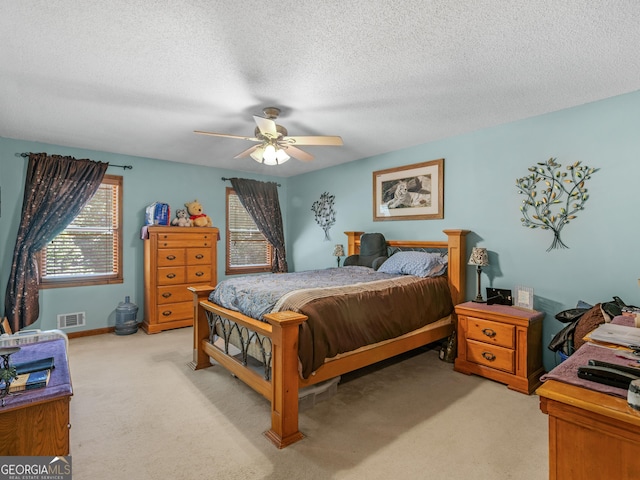 bedroom with multiple windows, visible vents, a textured ceiling, and light colored carpet