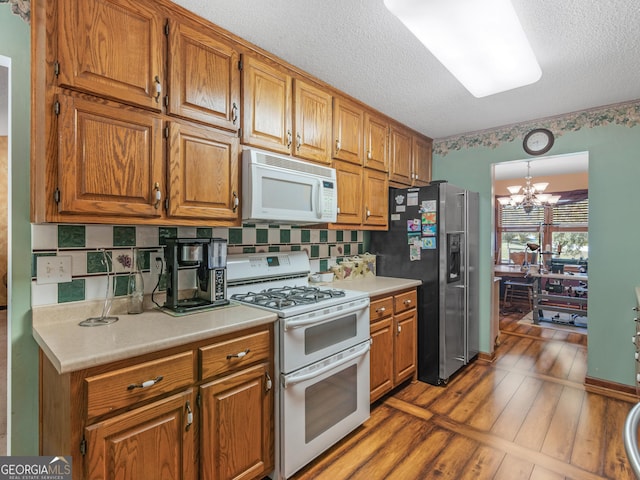 kitchen featuring white appliances, brown cabinetry, wood finished floors, an inviting chandelier, and light countertops