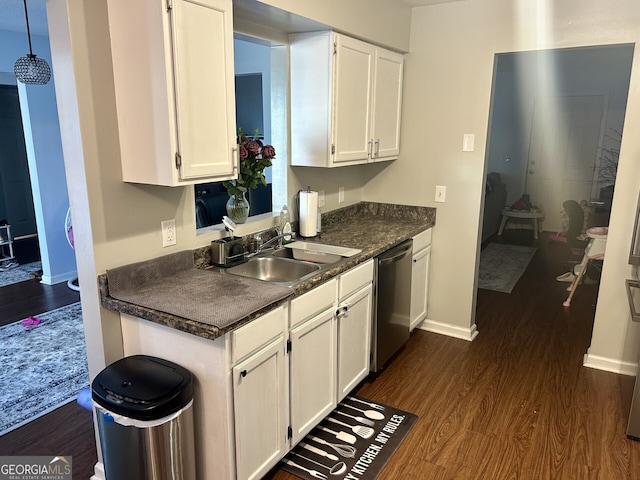 kitchen featuring dark wood finished floors, dark countertops, white cabinetry, a sink, and dishwasher