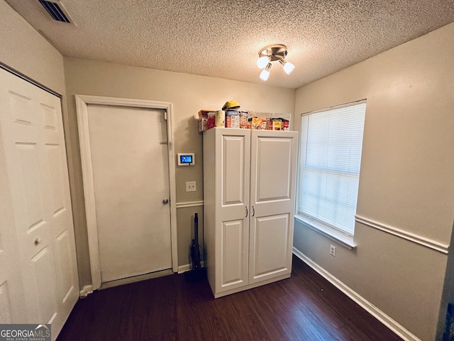 unfurnished bedroom with baseboards, visible vents, dark wood finished floors, and a textured ceiling