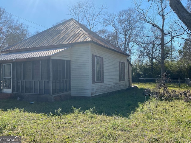 view of home's exterior featuring a sunroom, fence, metal roof, and a yard