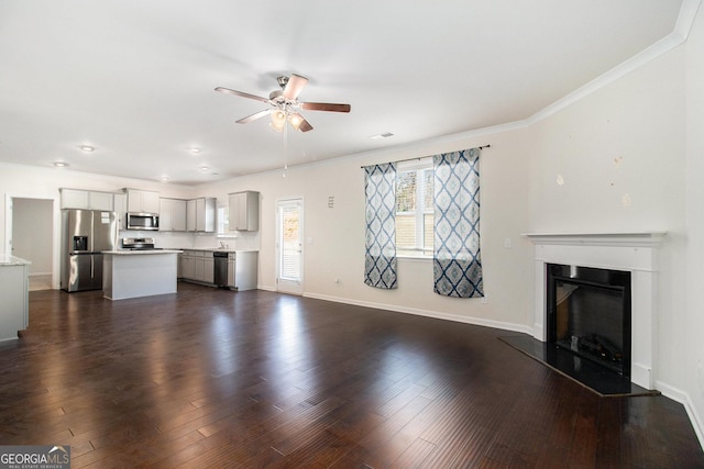 unfurnished living room featuring baseboards, a fireplace with raised hearth, ceiling fan, ornamental molding, and dark wood-type flooring