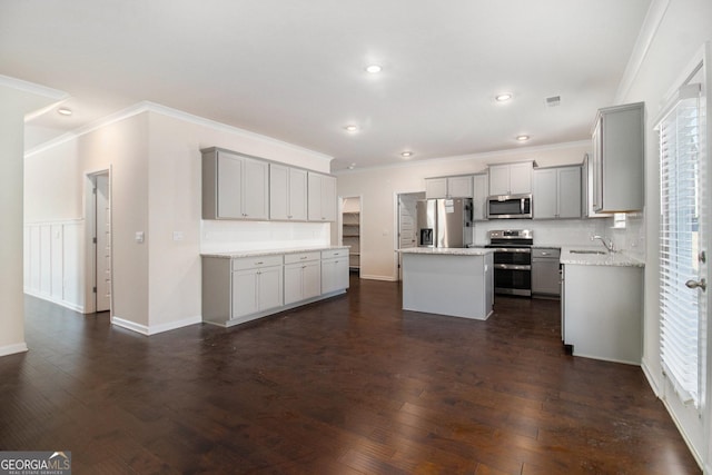 kitchen featuring dark wood finished floors, gray cabinetry, appliances with stainless steel finishes, a sink, and a kitchen island