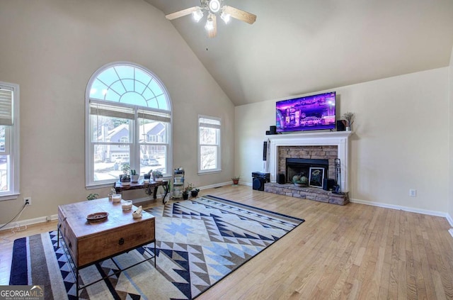 living area featuring high vaulted ceiling, a stone fireplace, baseboards, and wood finished floors