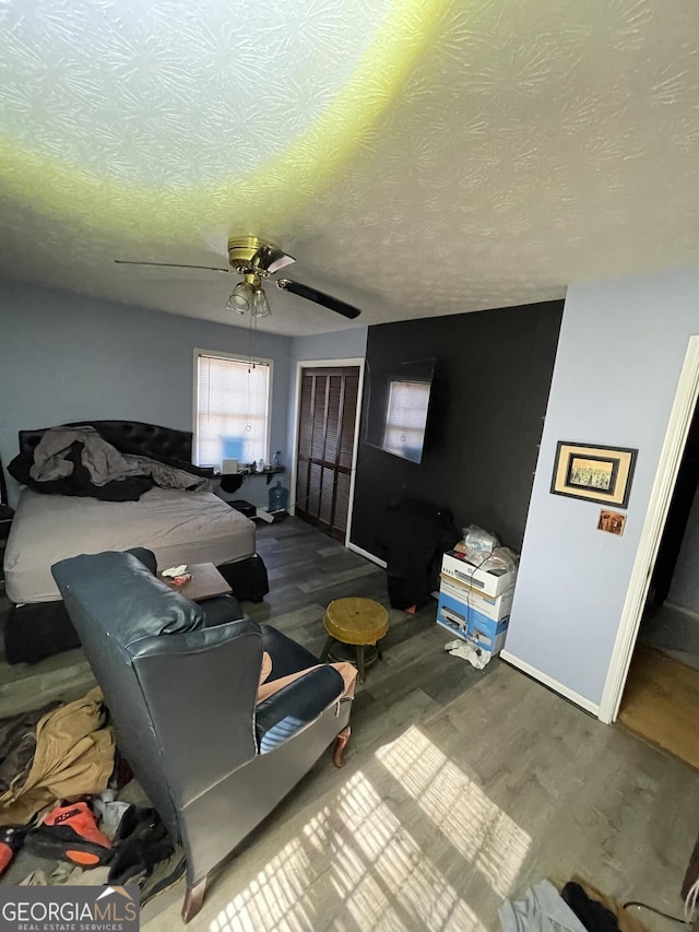 bedroom with baseboards, a ceiling fan, wood finished floors, a textured ceiling, and a closet