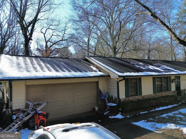 view of snow covered exterior with an attached garage and a shingled roof