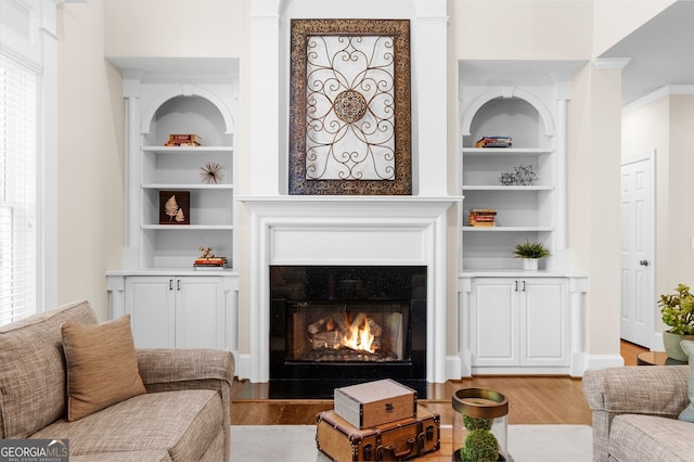 living room featuring light wood-type flooring, a healthy amount of sunlight, a lit fireplace, and built in shelves