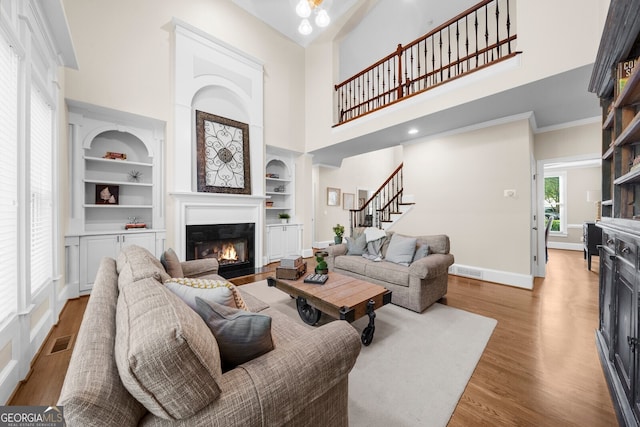 living room with built in features, visible vents, light wood-style floors, a glass covered fireplace, and baseboards