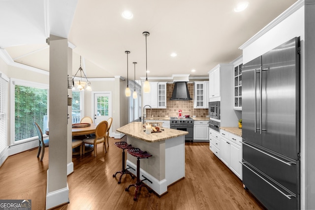 kitchen featuring built in appliances, wall chimney exhaust hood, ornamental molding, and dark wood-style floors