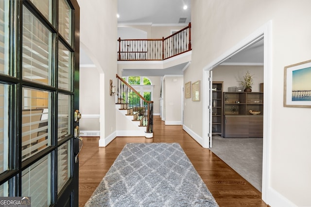 entryway with crown molding, a high ceiling, baseboards, and dark wood-style flooring