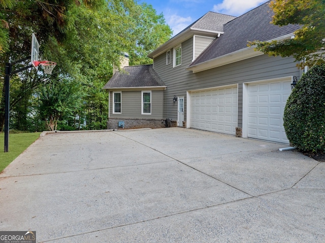 view of side of property with driveway, a shingled roof, a chimney, and an attached garage