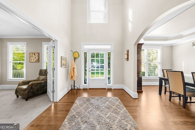 foyer with arched walkways, crown molding, baseboards, and wood finished floors