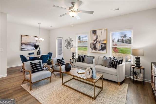 living area featuring dark wood-style floors, baseboards, visible vents, and ceiling fan with notable chandelier