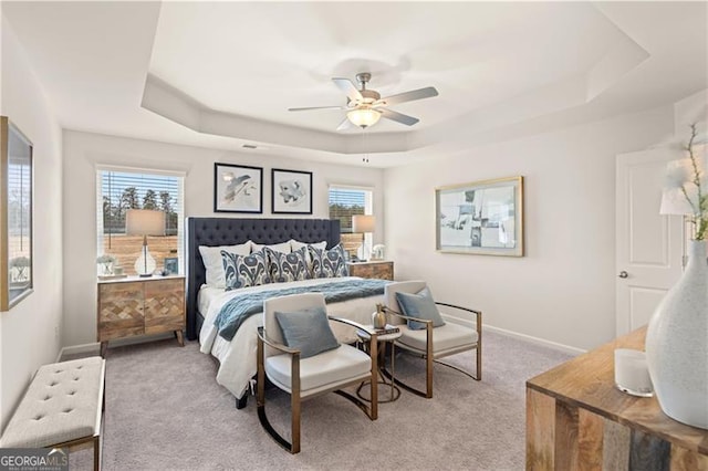 carpeted bedroom featuring a tray ceiling, ceiling fan, and baseboards