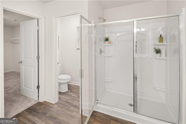 full bathroom featuring a spacious closet, a shower stall, toilet, and wood finished floors