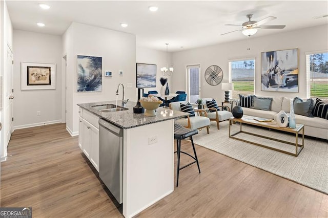 kitchen with stone countertops, a sink, open floor plan, stainless steel dishwasher, and a kitchen bar