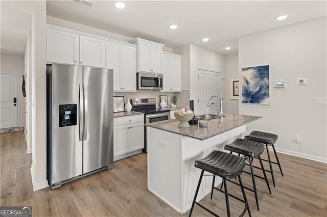 kitchen with stainless steel appliances, a sink, white cabinets, light wood finished floors, and a center island with sink