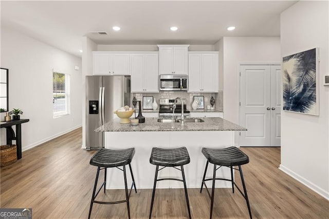 kitchen featuring appliances with stainless steel finishes, a sink, a kitchen island with sink, and white cabinets