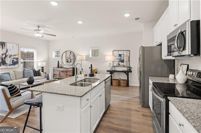 kitchen featuring stainless steel appliances, a kitchen island with sink, white cabinets, a sink, and wood finished floors