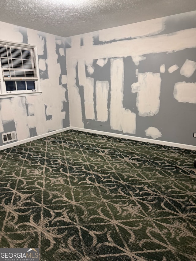 carpeted spare room with a textured ceiling, visible vents, and baseboards