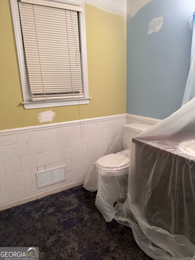 bathroom with tile walls, a wainscoted wall, visible vents, and toilet
