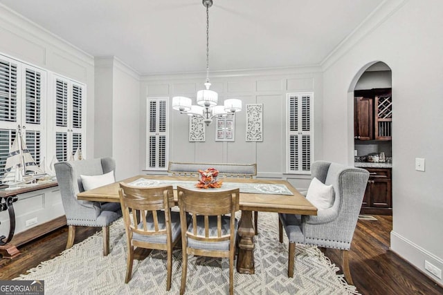 dining area with ornamental molding, a chandelier, dark wood-type flooring, and a decorative wall