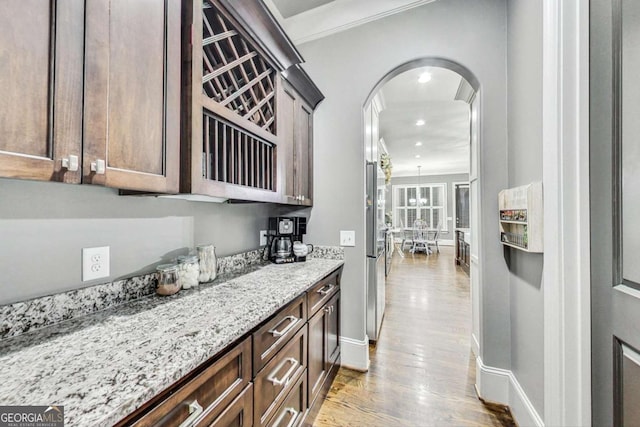 bar featuring arched walkways, wood finished floors, baseboards, freestanding refrigerator, and crown molding