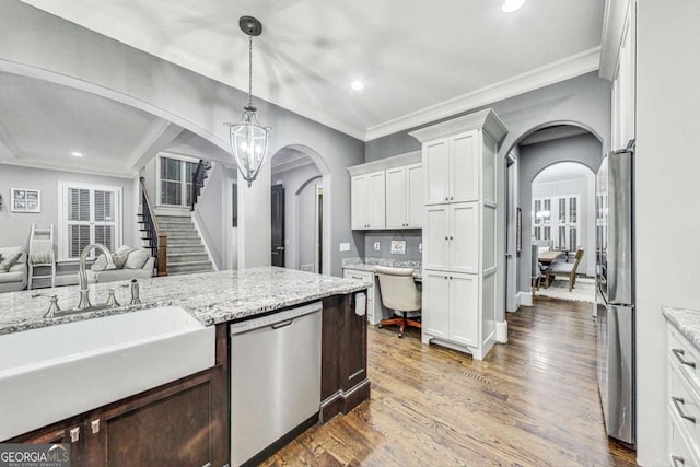 kitchen featuring arched walkways, appliances with stainless steel finishes, open floor plan, dark wood-type flooring, and a sink