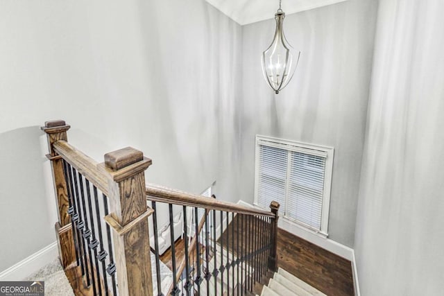 staircase featuring a chandelier, wood finished floors, visible vents, and baseboards