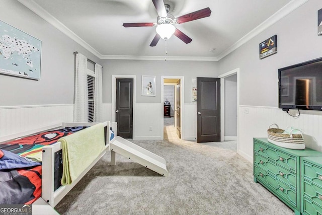 carpeted bedroom featuring a wainscoted wall, ornamental molding, and a ceiling fan