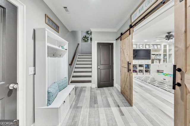 mudroom featuring a barn door, visible vents, ornamental molding, and wood finished floors